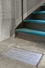 Das Bild zeigt die vier untersten Stufen der dunkelgrauen Metalltreppe und die Grundsteinplatte. Die gläsernen Oberflächen der Treppenstufen leuchten blau im Licht des Fotografen.