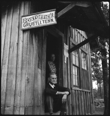 Woman and man in a wooden house with a sign saying "Postoffice Gruetli. Tenn.”