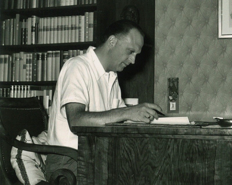 Hans Walter an seinem Schreibtisch in Buchillon, im Hintergrund  Büchergestelle